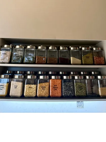 A clean, minimalist pantry cabinet with two shelves of decanted dals and grains. The uniform containers and ample space between them create a feeling of calm and order.