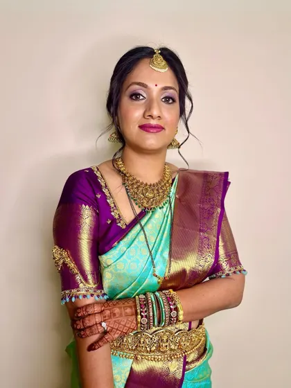 A beautiful reception look for a South Indian bride. The makeup is glamorous, with smokey eyes and a bold lip that complements her turquoise and purple saree.