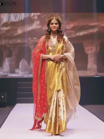 A regal look on the runway in a golden saree with a red and gold dupatta. The model's confident stance and the richness of the fabric create a truly majestic image.