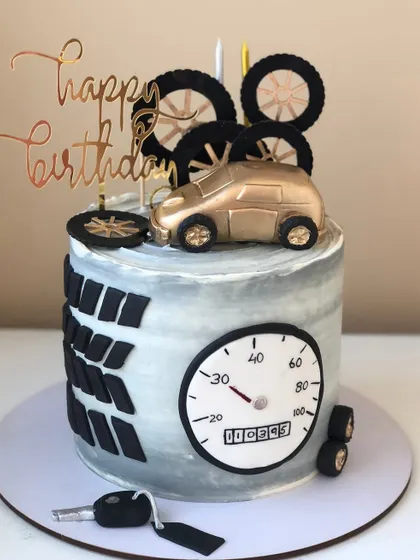 A sophisticated car-themed cake with a speedometer, tire treads, and a golden car topper.