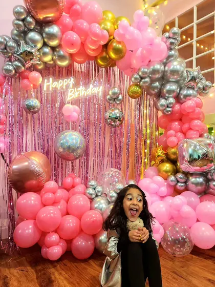 A party guest enjoying the shiny disco balls and vibrant pink balloon setup. It's all about creating an exciting and photo-worthy environment.