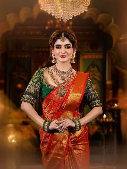 A regal and traditional bridal look featuring a rich red and green Kanjivaram saree. The makeup is defined by warm, shimmery eyes and a deep red lip, perfectly accessorized with temple jewelry.
