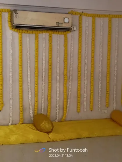 For indoor Haldi functions, a simple wall decoration with alternating strings of yellow and white flowers looks elegant.