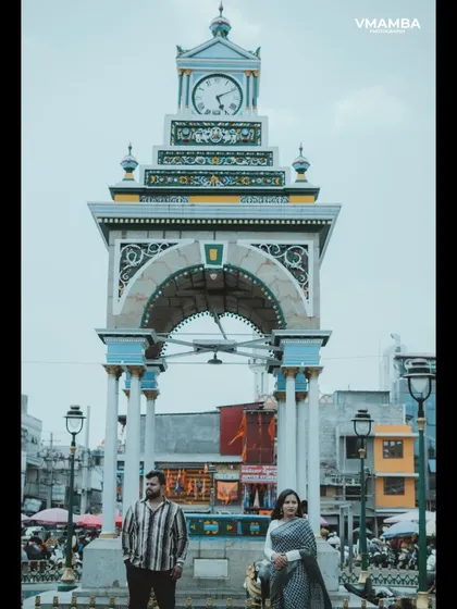 A vertical composition of a couple standing before a grand clock tower, emphasizing the scale and history of the location for their pre-wedding shoot.