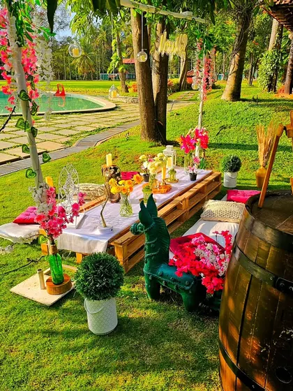 A colorful poolside picnic setup in a lush green resort. The low wooden pallet table is adorned with vibrant flowers, creating a perfect setting for a daytime celebration.