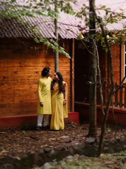 A couple in matching yellow outfits during their Haldi ceremony, captured in a rustic, natural setting.