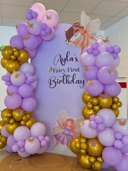 A 'Fairy First Birthday' theme with a purple and gold balloon garland framing a custom arched backdrop.