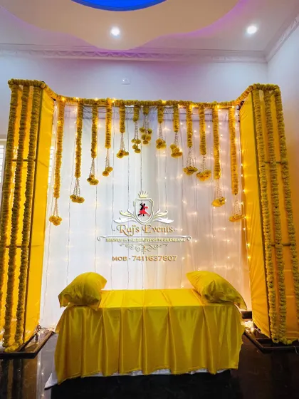 A simple and elegant Haldi ceremony setup for an indoor space. We used a white backdrop with hanging marigold strings and warm fairy lights to create a bright and cheerful ambiance.