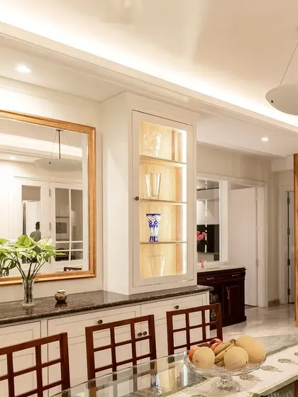 The dining area's display cabinets also function as a buffet counter. We used ambient lighting in both the white PU cabinets and the wooden niches to create a warm and layered effect.