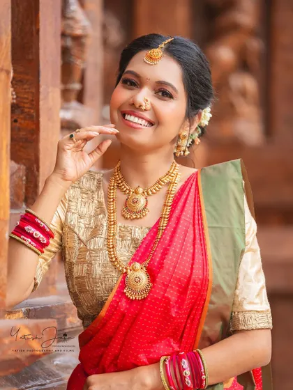 A joyful smile for Ganesh Chaturthi. The makeup is traditional and radiant, featuring a classic nose ring and gold jewelry that complements her red and gold saree.