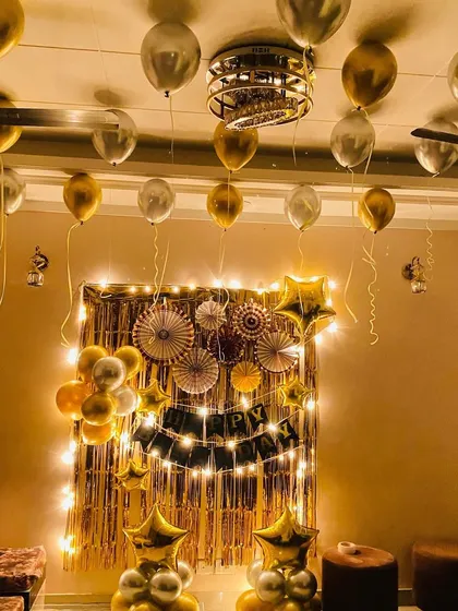 A sophisticated birthday decoration in a living room, featuring a gold and silver theme with a foil curtain and star balloons.