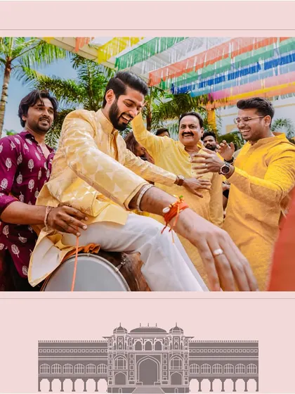 The groom having a blast during his haldi, playfully sitting on a dhol, surrounded by his laughing friends and family.
