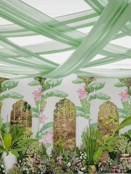 A beautiful backdrop for a Mehendi ceremony, with a hand-painted lotus design and lush greenery creating a garden-like feel.