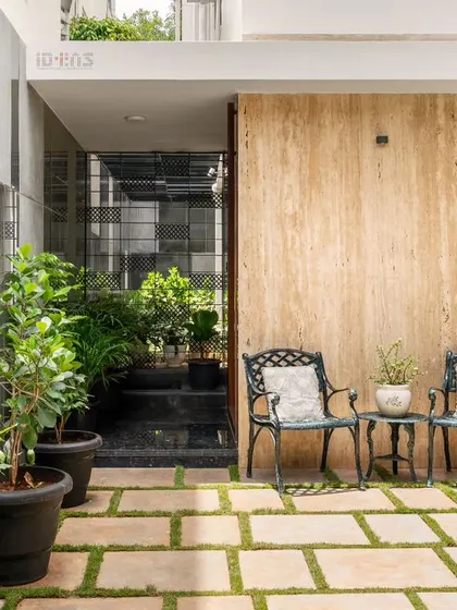 A quiet seating nook in an outdoor transition space at the Prakash Reddy residence. The combination of natural stone flooring, a travertine wall, and potted plants creates a peaceful corner to relax.