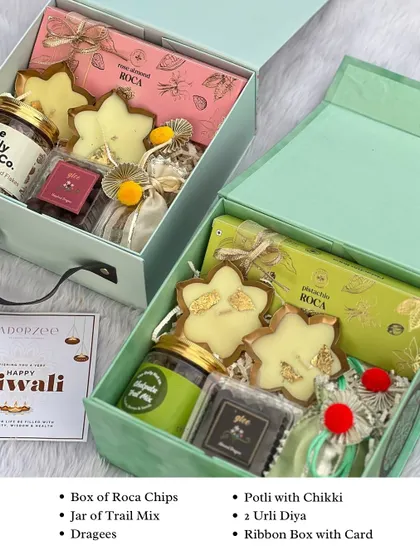 Our elegant twin box hamper is perfect for Diwali. This one is filled with Roca chips, a jar of trail mix, dragees, chikki in a potli, and decorative urlis, making it a complete festive package.