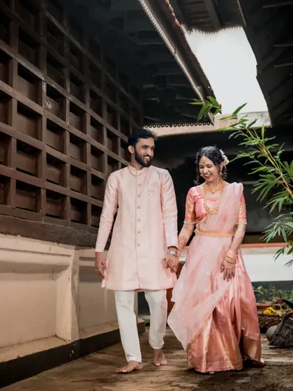 A happy, candid shot of a couple walking barefoot and hand-in-hand during their engagement ceremony at a traditional venue.