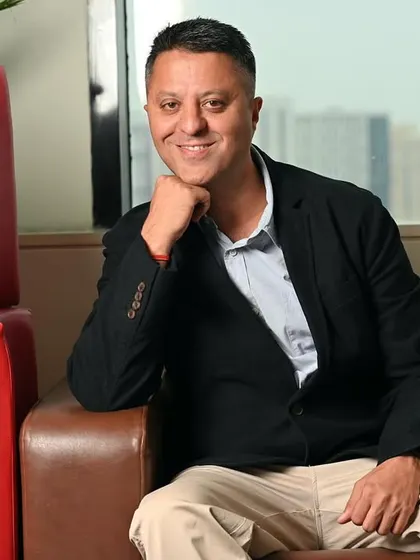 A relaxed yet professional portrait of a CEO on an office sofa. The city skyline in the background adds a sense of scale and ambition to the corporate headshot.