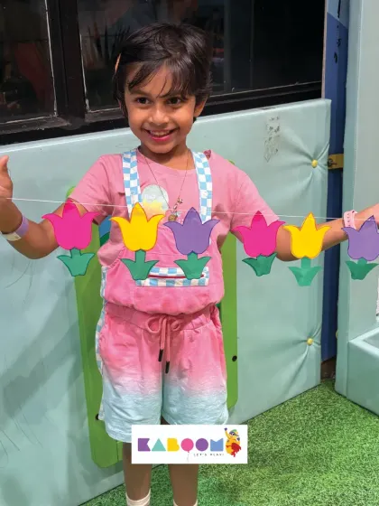 A smiling girl holds up her handcrafted toran, a string of colorful paper tulips she made herself. It’s a perfect decoration to take home and display.