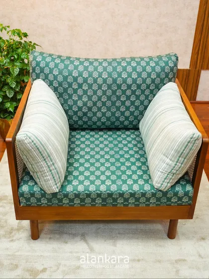 This single-seater sofa is a beautiful blend of materials, featuring a solid teak wood frame, cane side panels, and vibrant green patterned upholstery.