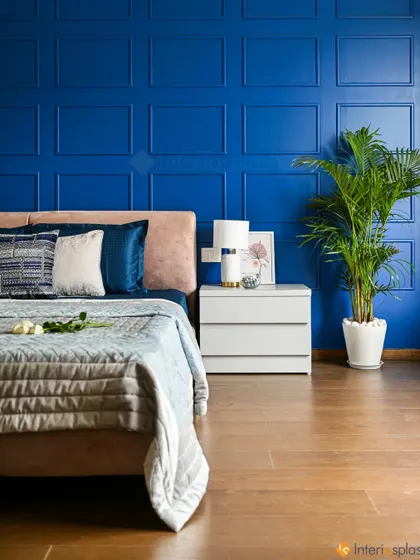 A bold and luxurious master bedroom with a royal blue accent wall featuring classic moulding. The peach-colored upholstered bed creates a beautiful color contrast.