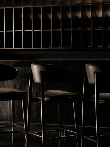 The bar area at Lair, a composition of shadow and minimal light. The design uses focused lighting to highlight the bottles and the dark, fluted bar front, creating a dramatic focal point.