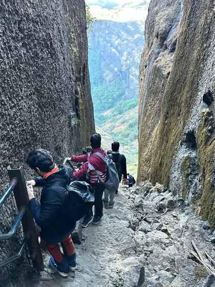 Descending through a narrow rock passage at Ratangad, known as the 'Needle Hole'. The fort's unique structure makes the trek exciting and varied.