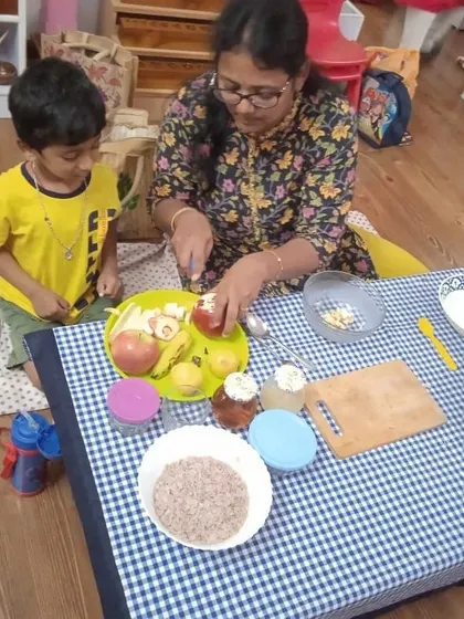 A parent demonstrates how to safely chop fruit while her child watches. These sessions empower both children and parents, sharing skills that can be practiced at home.