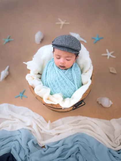A sleepy sailor adrift on a calm sea. We use soft fabrics to create a gentle wave effect for this nautical-themed newborn shot.