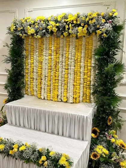 A bright and cheerful setup for any celebration, this backdrop uses strings of fresh yellow and white flowers, framed with dense greenery.