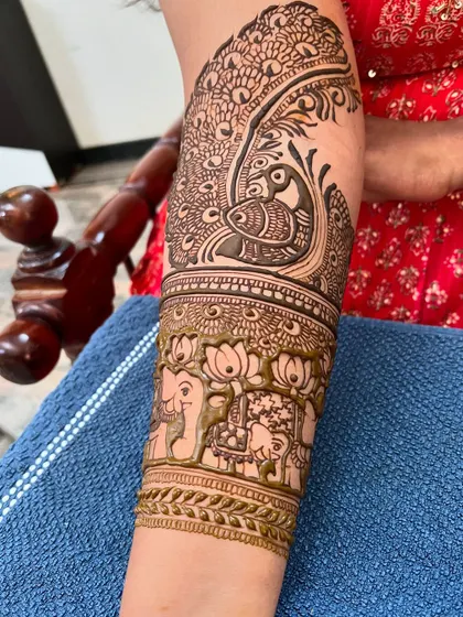 A close-up of a bridal arm piece, featuring a large peacock surrounded by lotus and elephant motifs.