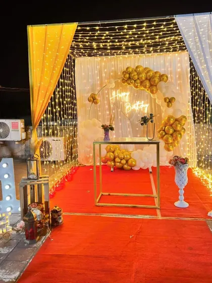 A simple yet stunning terrace decor setup. The canopy of fairy lights and a gold and white balloon arrangement create a magical ambiance for a birthday celebration.