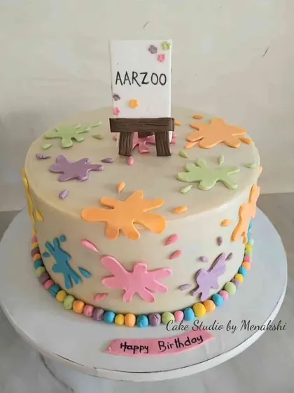 A cute art themed cake for someone who loves to paint. The cake is decorated with colourful paint splatters and a miniature easel.
