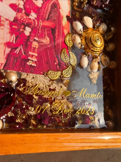 A close-up detail of a teakwood frame preserving a client's wedding varmala and kaleera. The golden accents and names add a touch of luxury to this personal keepsake.