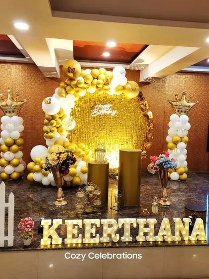 A royal-themed birthday party with a gold sequin backdrop, balloon pillars topped with crowns, and a personalized light-up name sign.