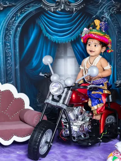Our little Krishna is enjoying his ride on a toy motorcycle, blending tradition with modern fun.