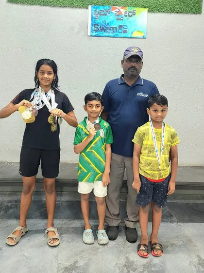 Kavya Karthik and other junior swimmers with their coach, showcasing their medals from the Skype Fitness interschool competition.