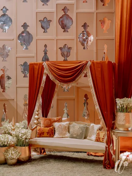 A regal seating canopy draped in rich orange velvet. The backdrop features a wall of custom-cut mirrors, reflecting the light and adding to the sense of grandeur.