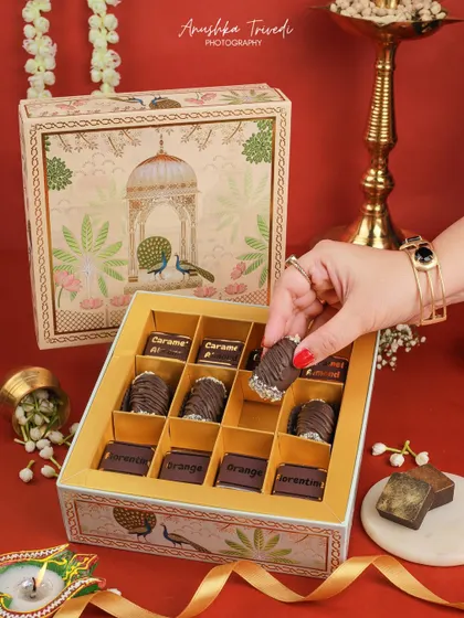 A lifestyle shot showing a hand selecting a chocolate from a festive box, making the product look interactive and desirable.