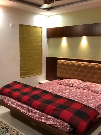 A simple yet elegant bedroom setup with a focus on lighting. A tufted headboard is set against a wood-panelled wall with three focused spotlights, creating a warm and inviting ambiance perfect for relaxation.