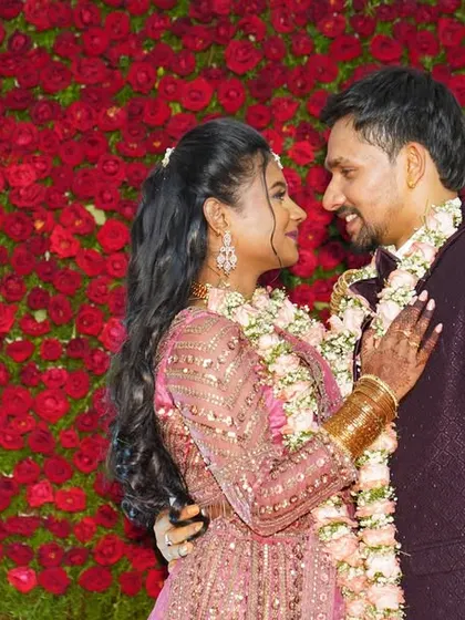A candid moment of a couple sharing a look in front of a stunning wall of red roses at their wedding reception.