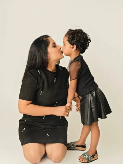 A sweet kiss between mother and daughter. This simple and modern studio shot in matching black outfits focuses on the pure love and affection in this beautiful bond.