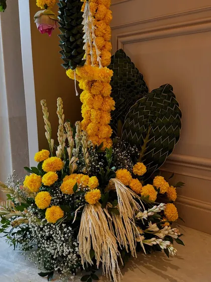A beautiful floor arrangement for a housewarming, combining vibrant marigolds with woven palm leaves and other traditional greens for a festive and auspicious look.