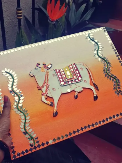 Holding the completed cow Lippan art. The piece has a lovely gradient background and detailed mirror work.