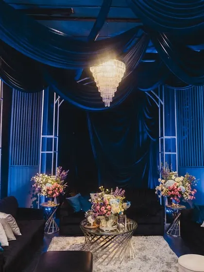 A chic lounge area for guests at the Sangeet, featuring deep blue velvet sofas, modern white structures, and elegant chandeliers.