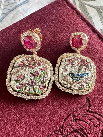 The cherry blossom and bluebird micromosaic earrings, resting on a jewelry box. This image showcases the rich colors and fine details of the handcrafted artwork, set in 18k gold with rubies.