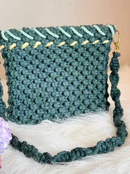 A unique design in a deep teal, this handbag features a decorative woven edge in light green and yellow. The twisted strap and gold-tone hardware add an elegant finishing touch.