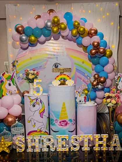A vibrant unicorn theme for a 5th birthday, featuring a circular backdrop, a light-up number '5', and unicorn-themed plinths for the cake display.