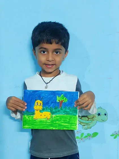 This student is happy to show off his colorful drawing of a friendly giraffe in a green landscape.