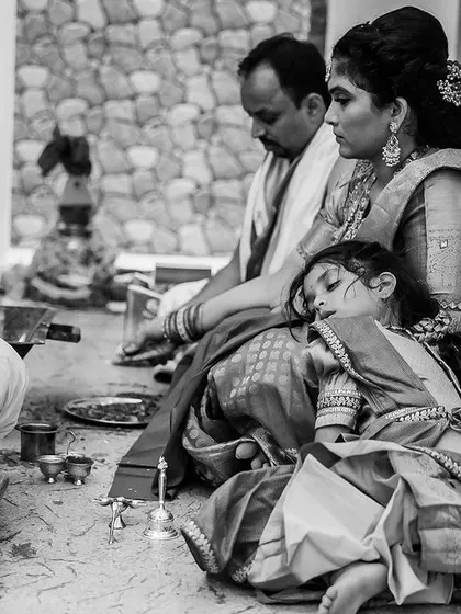 A candid black and white photo of a little girl who has fallen asleep on her mother's lap during the long puja. A sweet, real-life moment.