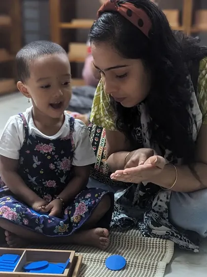 A teacher and a young child share a moment of delight while exploring geometric shape insets. The child's expression shows the pure joy that comes from discovery and connection.